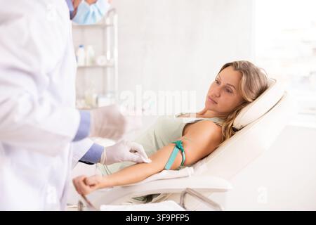 Unrecognizable male senior nurse performs procedure of blood drawing for analysis to woman Stock Photo