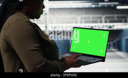 Admin in data center using app on green screen laptop to ensure error free mainframes networks. IT specialist uses mockup notebook to monitor server hub gear parts for failures, camera B Stock Photo