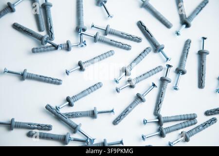 A lot of gray plastic dowels with screwed screws are chaotically scattered on a white background Stock Photo