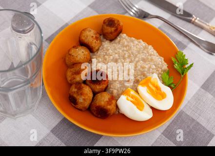 Homemade breakfast is served on plate - small portion of oatmeal, stewed meatballs and boiled egg Stock Photo