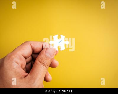 Hand holding a puzzle piece with blue check mark. Business solutions, perfect fit, problem solving, talent acquisition, quality management, strategic Stock Photo