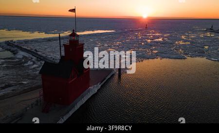 Aerial view of Big Red lighthouse surrounded by ice floes on Lake Michigan during a vibrant sunset in Holland, Michigan, United States. Stock Photo