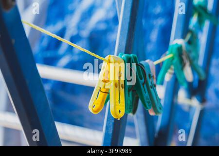 Close up view of colorful yellow and green plastic clothespins hanging on a yellow line against a blue background. Stock Photo