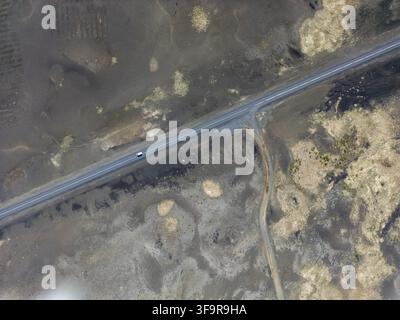 Aerial view of a lonely road cutting through a vast volcanic landscape with dark lava fields and sparse vegetation in Iceland. Stock Photo