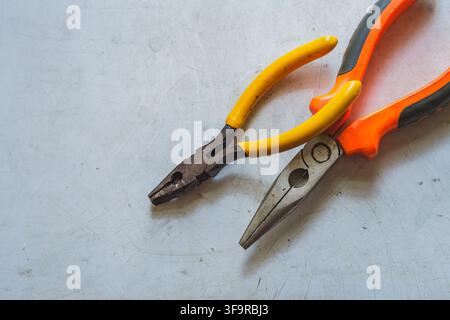 High angle view of two different pairs of pliers with yellow and orange handles resting on a scratched white workbench. Stock Photo