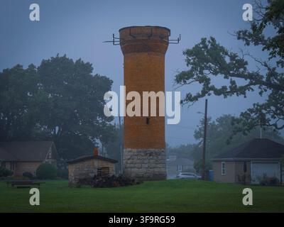 Historic old brick and stone water tower standing tall in a foggy park surrounded by suburban houses in Naperville Illinois Stock Photo