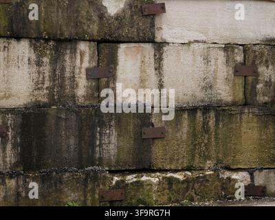 Close up of a weathered old concrete block wall with stained textures and rusty metal reinforcement plates Stock Photo