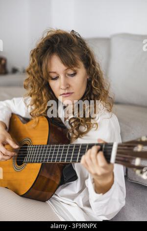Curly-haired woman focused on playing the guitar in a white shirt Stock Photo