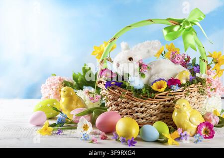 Easter composition with little white bunny in basket, chicks, spring flowers and colorful Easter eggs . Easter Card with copy space Stock Photo