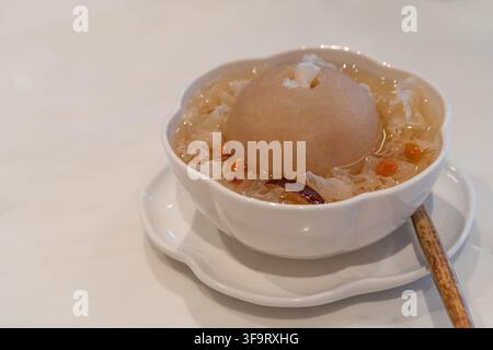 Traditional Chinese sweet dessert soup featuring a whole pear surrounded by snow fungus, dried red dates, and goji berries in a light sweet broth. Stock Photo