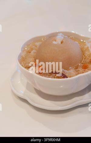 Traditional Chinese sweet dessert soup featuring a whole pear surrounded by snow fungus, dried red dates, and goji berries in a light sweet broth. Stock Photo
