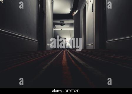 YORK, ENGLAND, DECEMBER 12, 2018: Exit fire sign hanging on ceiling on dark mysterious corridor in building near stairs. Door room perspective in lone Stock Photo