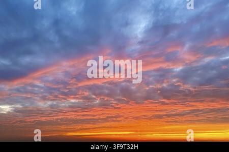 Stunning sunset sky filled with textured clouds glowing in shades of orange, pink, and blue, creating a dramatic and colorful natural background Stock Photo