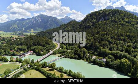Aerial shot of a turquoise river curving through a forested valley with mountain peaks under a sunny summer sky Stock Photo