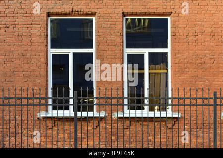 Two rectangular windows with white frame, on a background of wall of red brick. In the foreground is the iron fence. From the window of Saint Petersbu Stock Photo