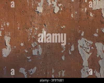 A close up view of an old weathered terracotta colored wall with chipped white paint patches showing organic decay and rustic textures. Stock Photo
