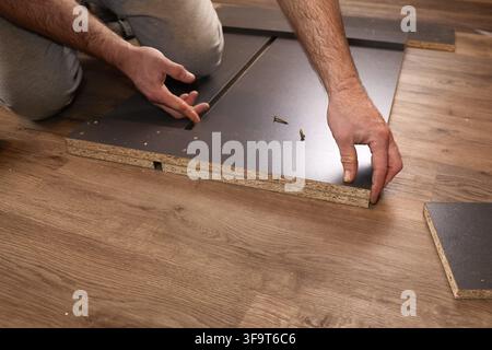 Man assembling furniture on wooden floor, connecting panels with screws. DIY home improvement and flat pack assembly concept Stock Photo