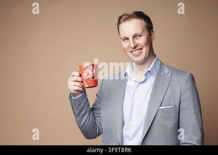 Studio portrait of determined successful businessman in suit and shirt holding red mug with positive slogan Everything is under control . He is smilin Stock Photo