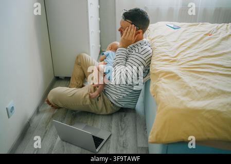 Stressed father experiencing emotional burnout and headaches while working from home, struggling with parenting duties and a crying baby, feeling overwhelmed by family and career demands Stock Photo