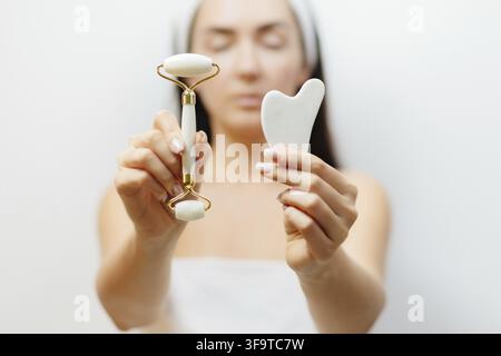 Natural Jade Face Lifting Gouache Scraper Massager. Beautiful Woman Using face roller and Gua Sha scraper over skin. beauty face skin care at home Stock Photo