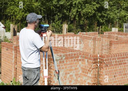 A construction worker checks the height level of the brickwork using a measuring tool on the construction site. Building a house Stock Photo