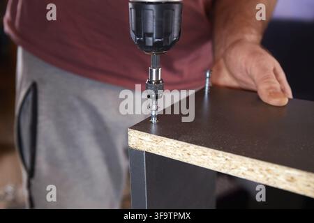 A man assembles furniture in his home workshop using a screwdriver Stock Photo
