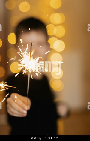 Fireworks close-up in the hands of a child, against the background of a yellow Christmas garland. Happy child with sparklers on New Years celebration Stock Photo
