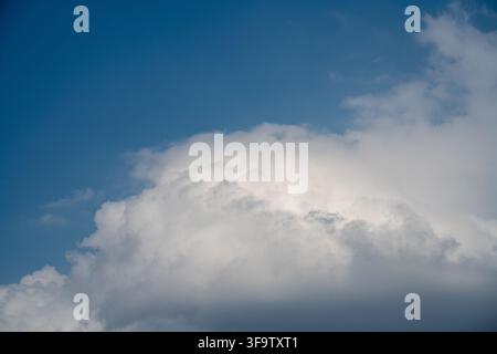 Thick clouds fill the sky, showing shades of white and gray. Sunlight breaks through, creating a bright view. This scene captures daytime clouds in a Stock Photo