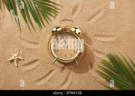 Alarm clock on a sandy beach. Noon, 12 p.m. A dangerous time for tanning and being in the sun.Sand texture, natural background. Top view Stock Photo
