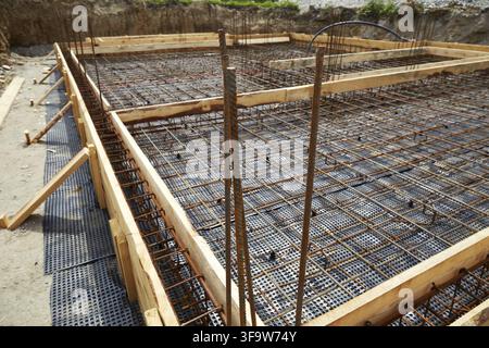 Reinforced concrete foundation preparation with steel rebar grid and wooden formwork in an excavation pit at a residential construction site Stock Photo