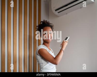 Young woman setting home temperature using air conditioner remote. Stock Photo
