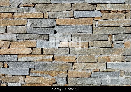 Wall made of  strips of  luserna stone with colors ranging from blue gray  to brown and golden yellow. Rustic coating for outdoor. Texture Stock Photo