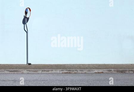 Traffic convex mirror on a pole with light blue plaster wall on behind. Sidewalk and street in front. Background for copy space. Stock Photo