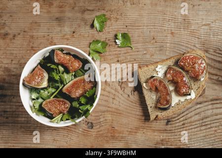 Salad of fresh figs and herbs in a white bowl on a wooden background. Toast with cheese and figs. A healthy green salad and a fresh fruit and vegetabl Stock Photo