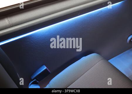 A car interior with blue ambient lighting, textured door panel and fabric seat creating modern travel atmosphere Stock Photo