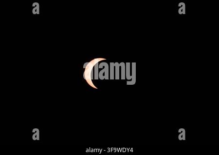 Telephoto photograph of a partial solar eclipse, capturing a crisp crescent-shaped sun as the moon partially covers the solar disk against a pure blac Stock Photo