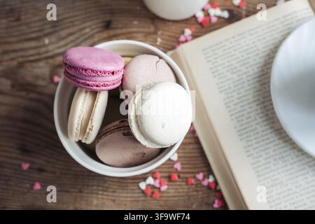 Macaroons in a bowl, a cup of coffee, on a background of small hearts on a wooden background Stock Photo