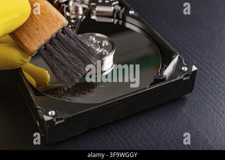 Cleaning the hard disk with a brush. Vacuuming old disk data on your computer. Dark background Stock Photo