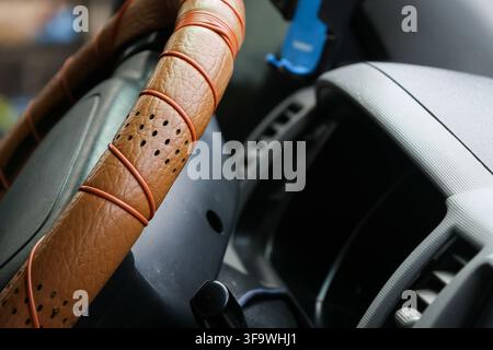 A leather steering wheel with perforated grip inside modern vehicle, detailed close up showing textured material, curved dashboard, air vent, and driv Stock Photo