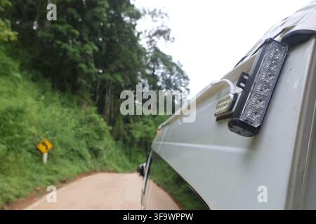 An off road vehicle on forest road with auxiliary light and side mirror, traveling through lush green woodland along winding unpaved route in adventur Stock Photo
