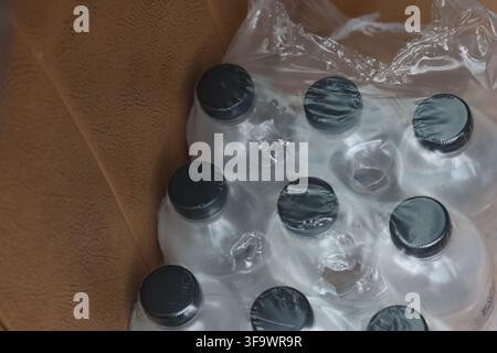A plastic bottle pack in clear shrink wrap on brown cardboard surface, showing black bottle cap detail and transparent packaging for disposable bevera Stock Photo