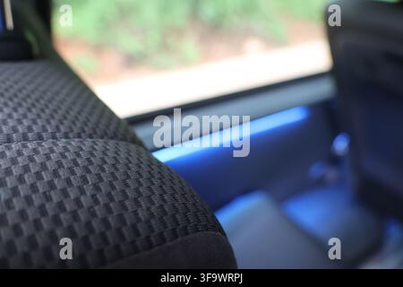 A textured fabric seat inside vehicle with blue ambient lighting and blurred outdoor scenery through window Stock Photo