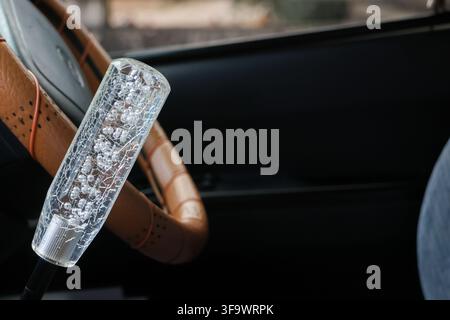 A transparent crystal gear shift knob inside vintage car with leather steering wheel, showcasing detailed texture and reflective design Stock Photo
