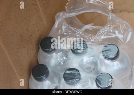 A transparent plastic water bottle pack with dark cap resting on brown leather surface, showing crinkled packaging and recycled material detail Stock Photo