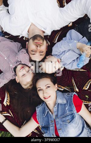 Above view of happy family lying in park together with kids smiling, playing, looking at camera. Positive parents with two son posing outdoor. Concept Stock Photo