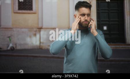 Man holding smartphone to ear, hand on forehead, standing on a street by a building entrance with cobblestone pavement; concern urgent call. Stock Photo