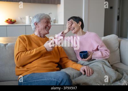 Joyful elderly couple enjoying conversation and funny stories sitting together at home on couch. Stock Photo