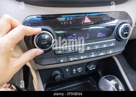 Driver hand turning the rotary temperature adjustment dial on a modern car interior central climate control console. Stock Photo