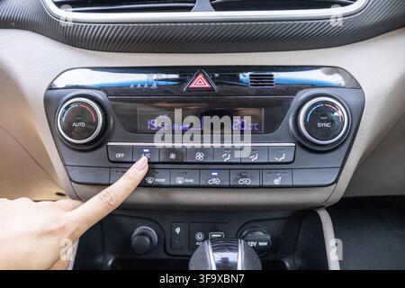 Front view of a finger pressing buttons on the central audio and AC console unit inside a contemporary passenger car. Stock Photo