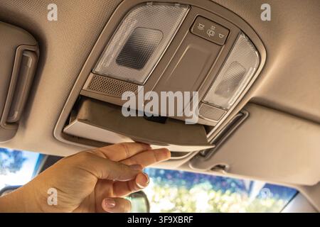 Hand pulling down the overhead sunglass storage compartment built into the car ceiling console. Stock Photo